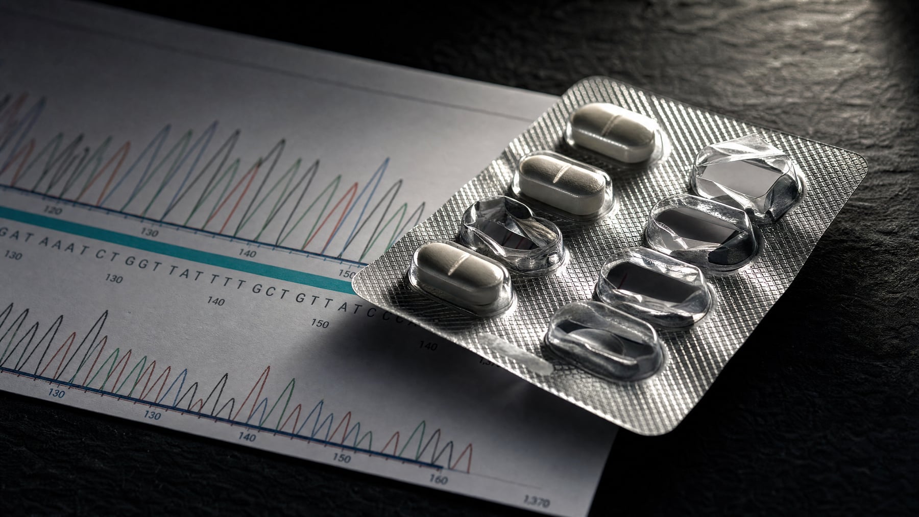 A half-emptied blister pack of tablets resting on a printed DNA sequencing trace, dramatic side light on the foil, illustrating antidepressant pharmacogenomics.