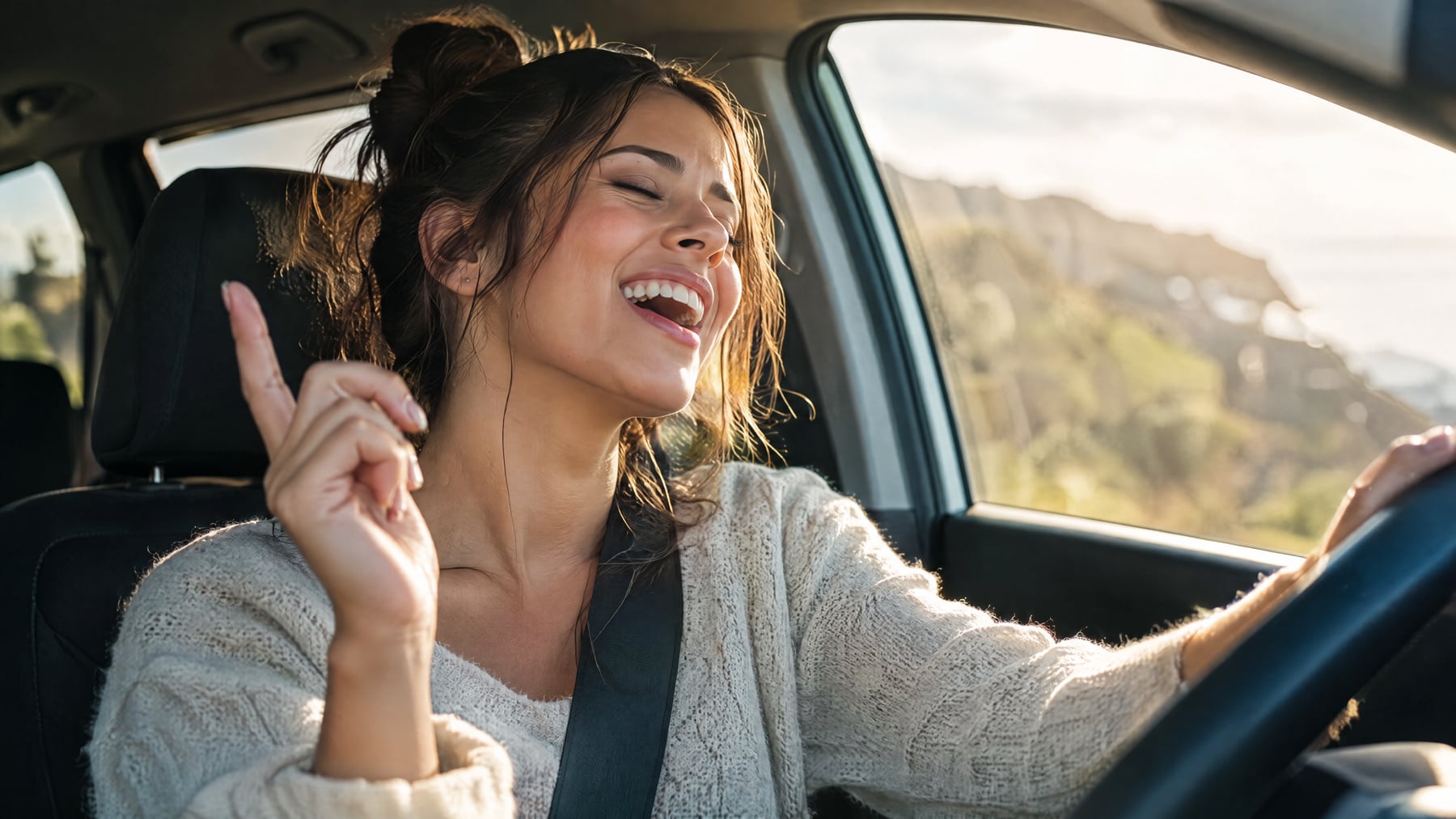 A woman singing joyfully with her eyes closed in the driver's seat of a car, sunlit coastline behind her, illustrating how singing builds vagus nerve tone.